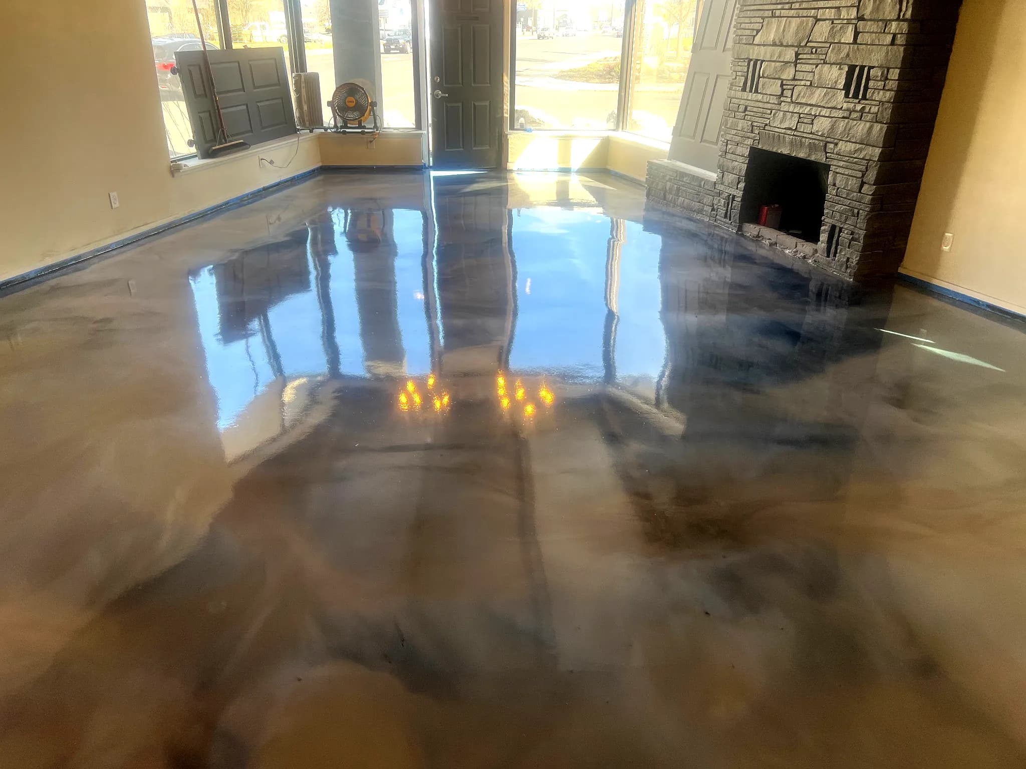 High-gloss metallic epoxy floor with deep reflections in a residential living room featuring large windows and a stone fireplace
