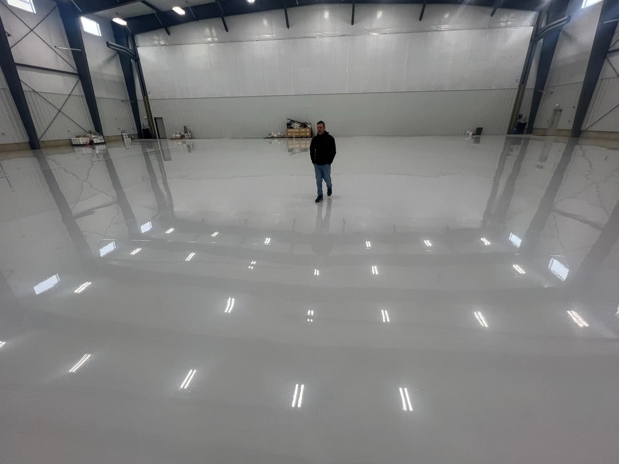 Large industrial space with a freshly finished high-gloss white epoxy floor and a single person standing at center