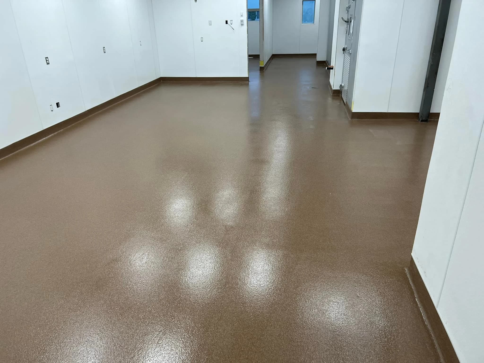 Durable brown textured epoxy floor in a commercial food-grade facility with clean white walls and walk-in cooler access