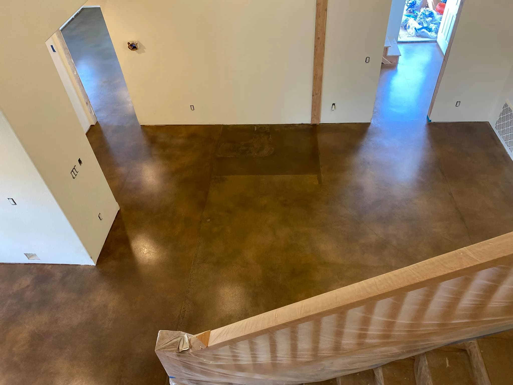 Warm-toned stained concrete floor in a new residential construction with exposed wood trim and unfinished walls
