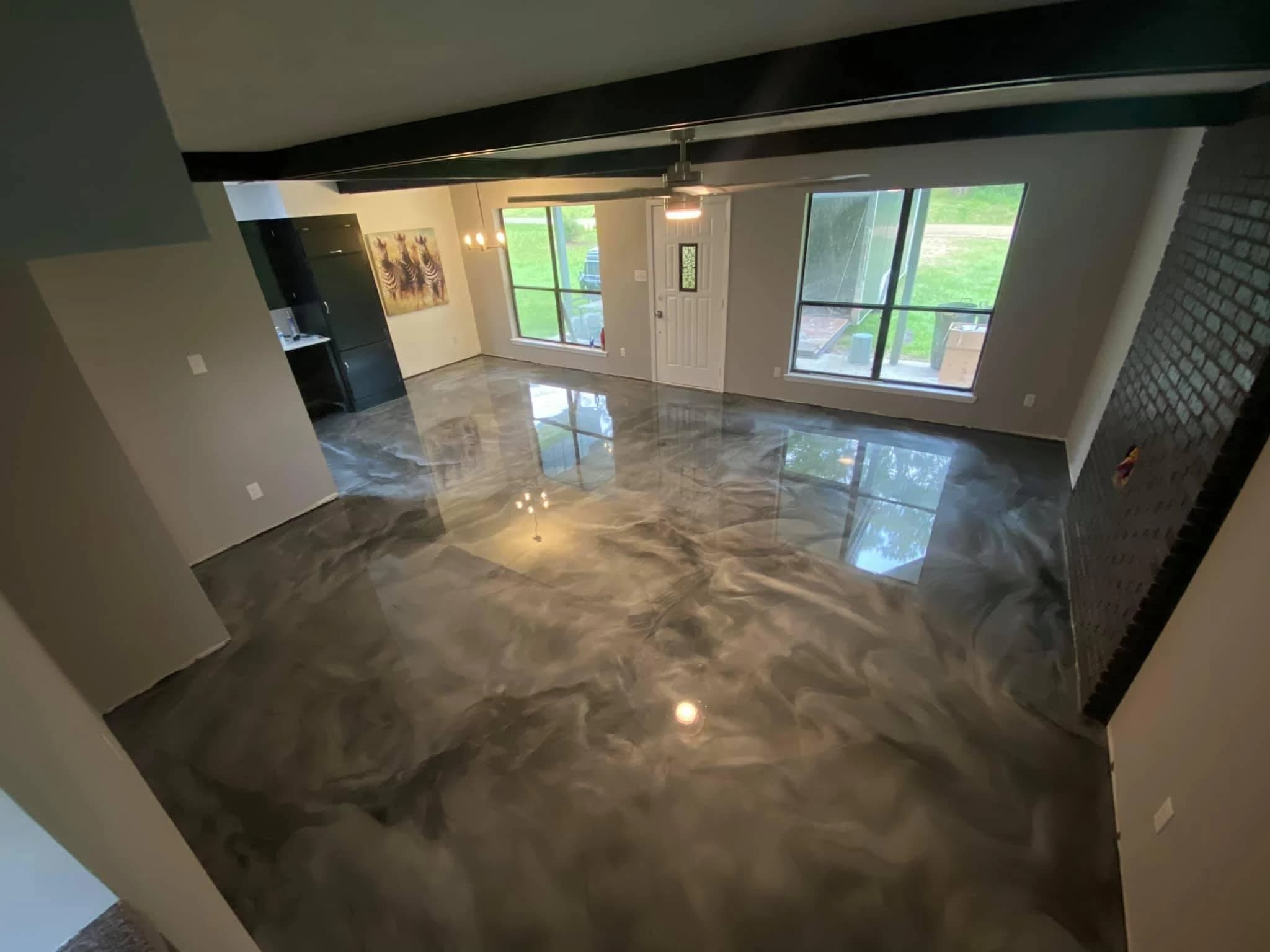 Polished black and gray metallic epoxy floor in a modern living space with large windows and minimal décor