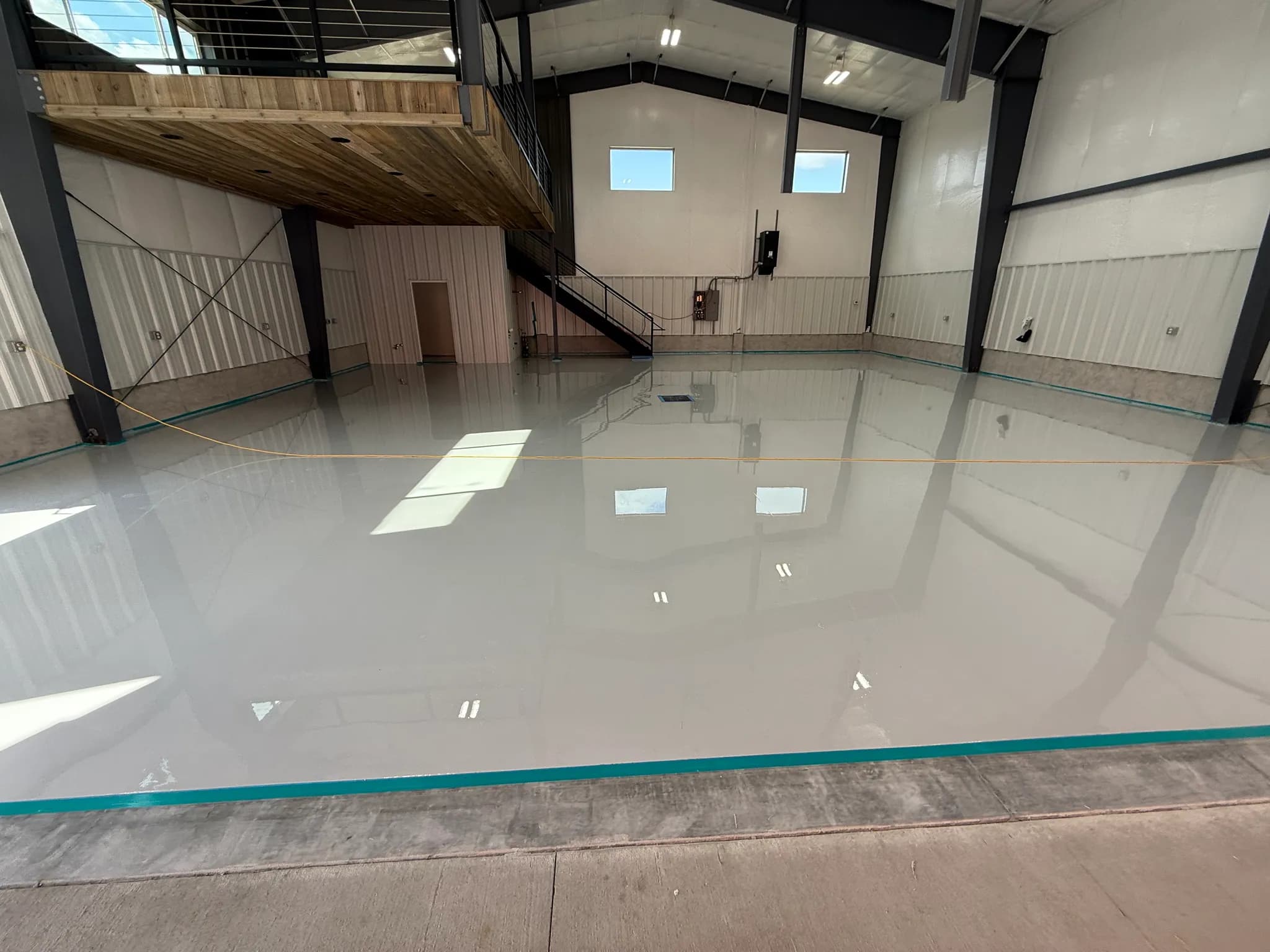 Finished high-gloss epoxy floor in an industrial warehouse with overhead loft and exposed steel beams