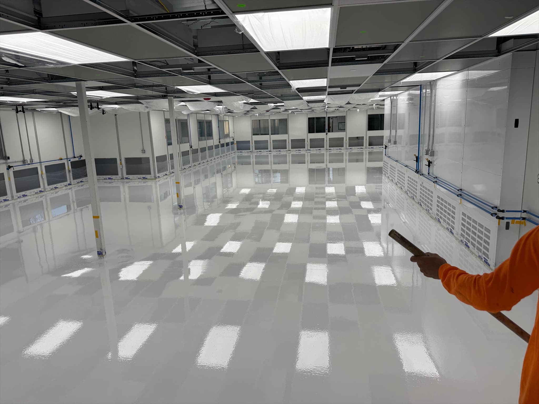 High-gloss white polymer flooring in a large industrial cleanroom facility with reflective surfaces