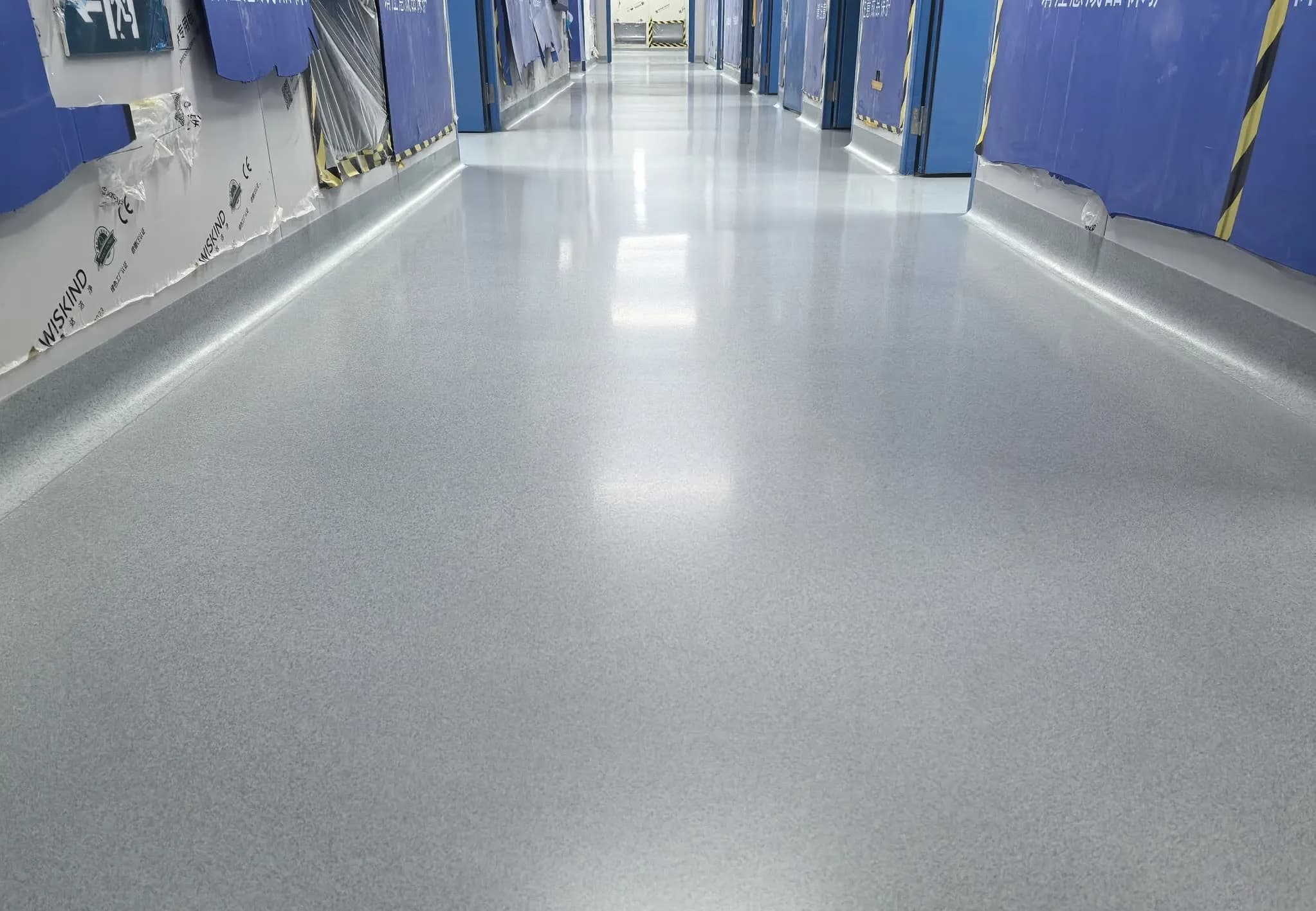Seamless gray epoxy floor in a clean, modern hallway of an industrial facility with protective plastic on the walls
